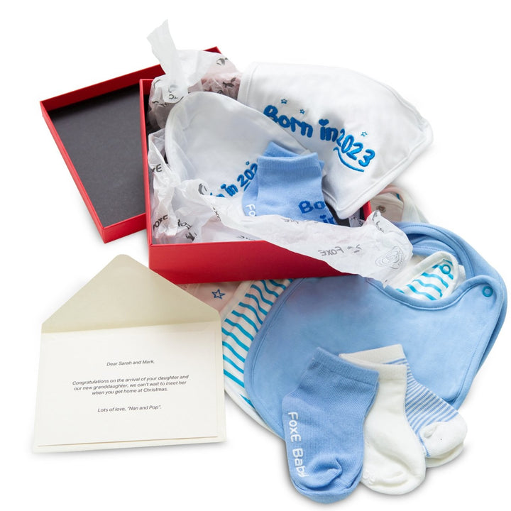 A blue Born In 2023 Gift Set including 4 bibs, 4 pairs of soft cotton socks, and a cute baby beanie, all packaged in a little gift box.