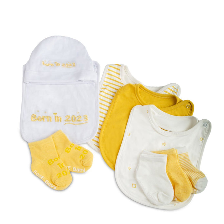 A yellow Born In 2023 Gift Set including 4 bibs, 4 pairs of soft cotton socks, and a cute baby beanie.