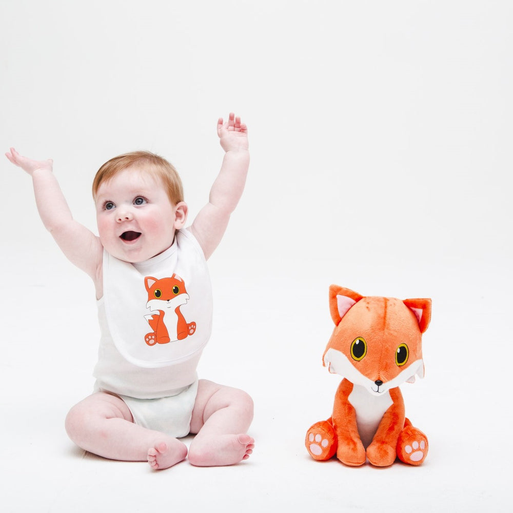 Cute little boy waving his arms in the air , wearing a Fox baby bib and sitting with a soft fox cuddle toy. 